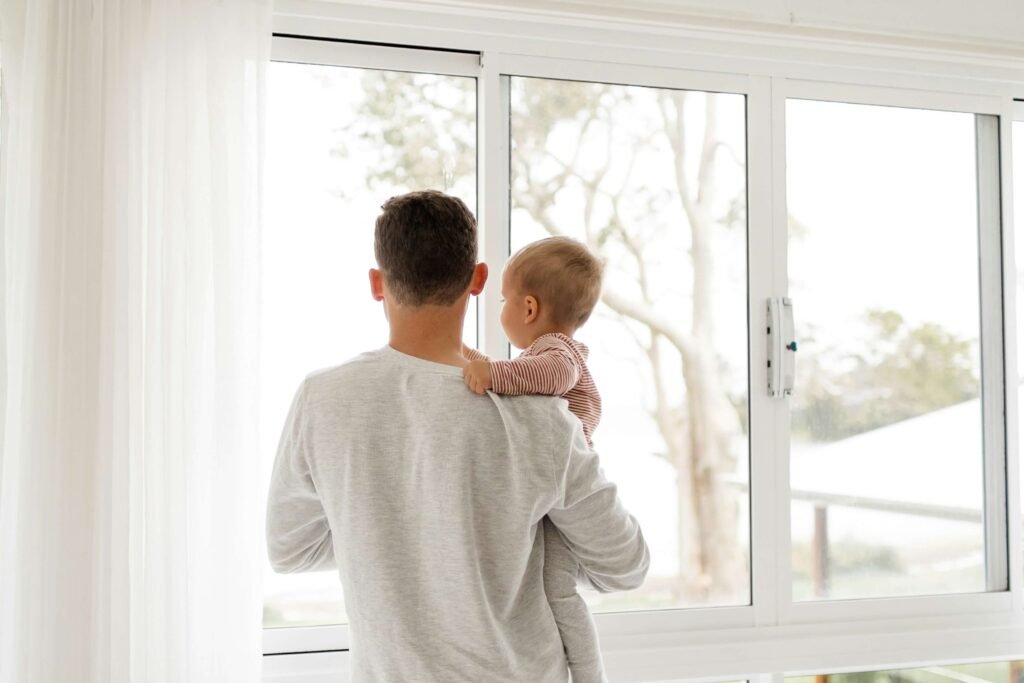 Parent and baby gazing out a sunlit window together, beginning the day with presence and connection showing daily rhythms for families
