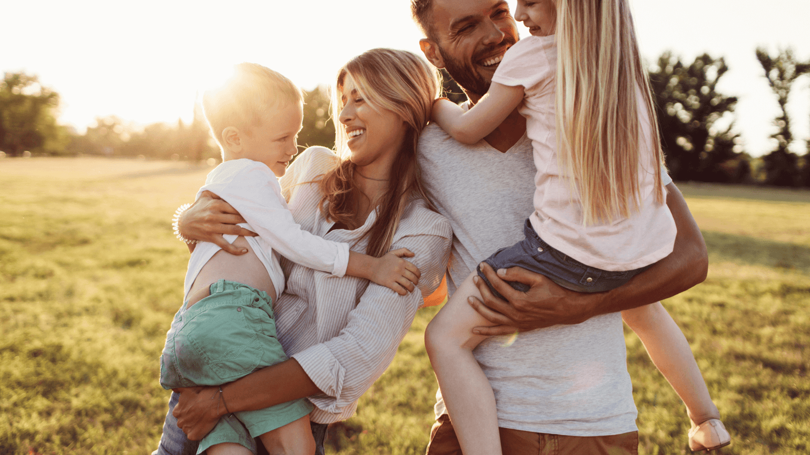 Blog Newsletter Signup Little Guru & Co. blog family of four laughing and holding children in a sunlit field symbolizing love and connection