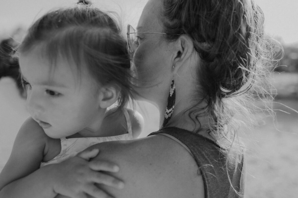 Home A mother holding her young daughter close, captured in soft natural light, symbolizing conscious parenting and emotional connection.