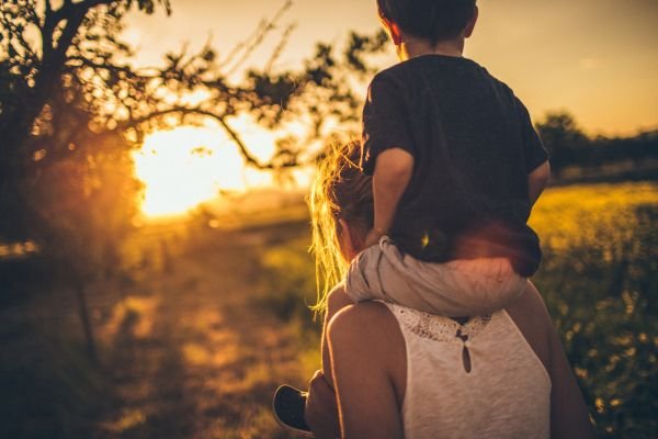 Guardians of Wonder: Preserving the Innocence of Childhood Parent carrying child on shoulders during sunset walk through a field, nurturing connection and presence.