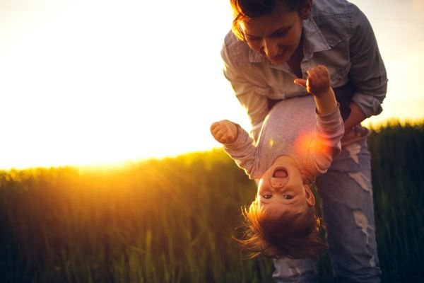 Guardians of Wonder: Preserving the Innocence of Childhood Mother holding child upside down in the sunlight, laughter and connection preserving the innocence of childhood.