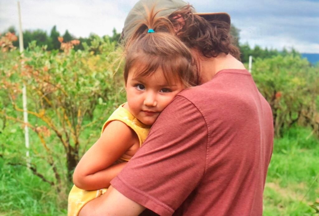 Toddler in a yellow dress hugging parent in a field, reflecting connection, love, and the values of a sustainable babywear brand.