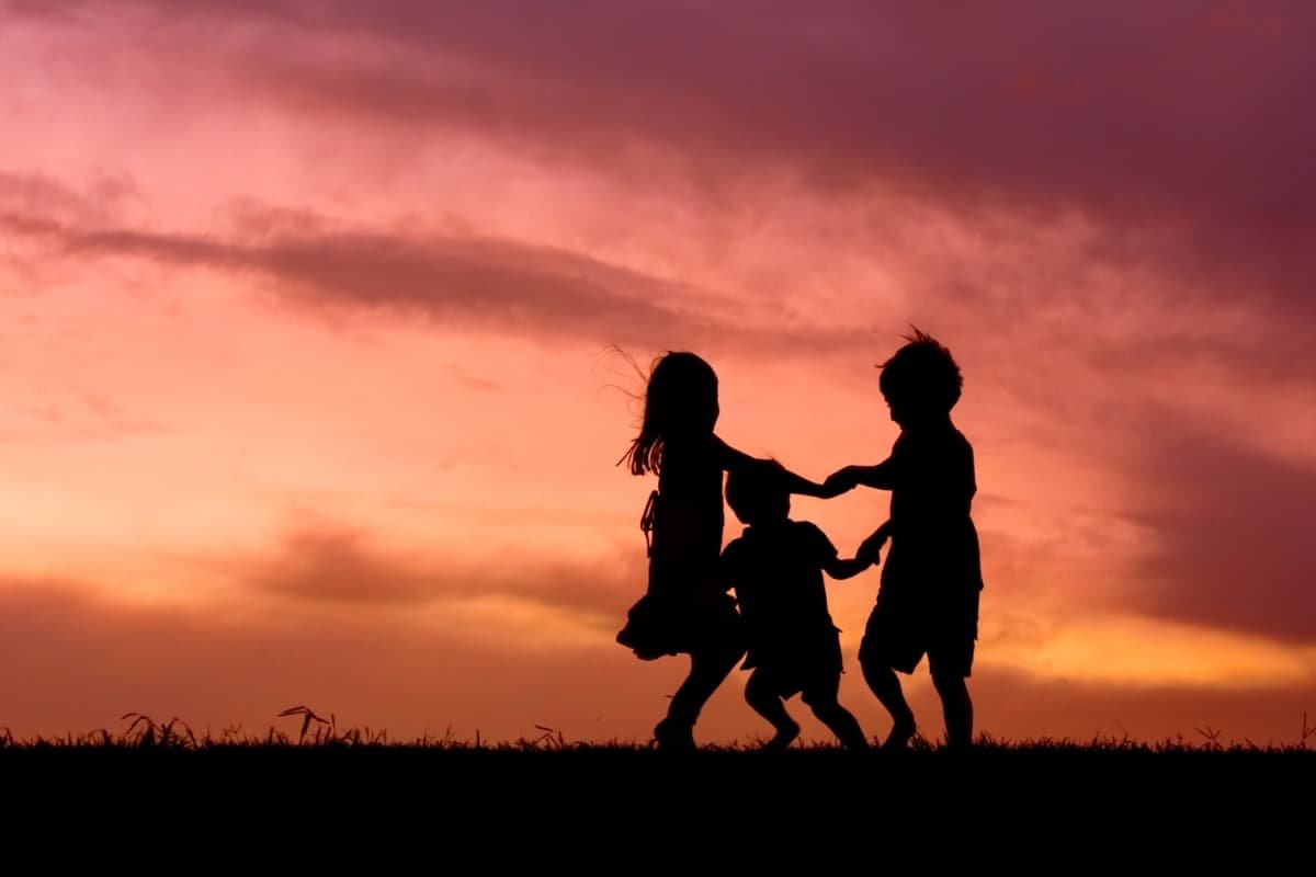 Children holding hands at sunset, representing connection, emotional development, and the sacred nature of early childhood relationships.