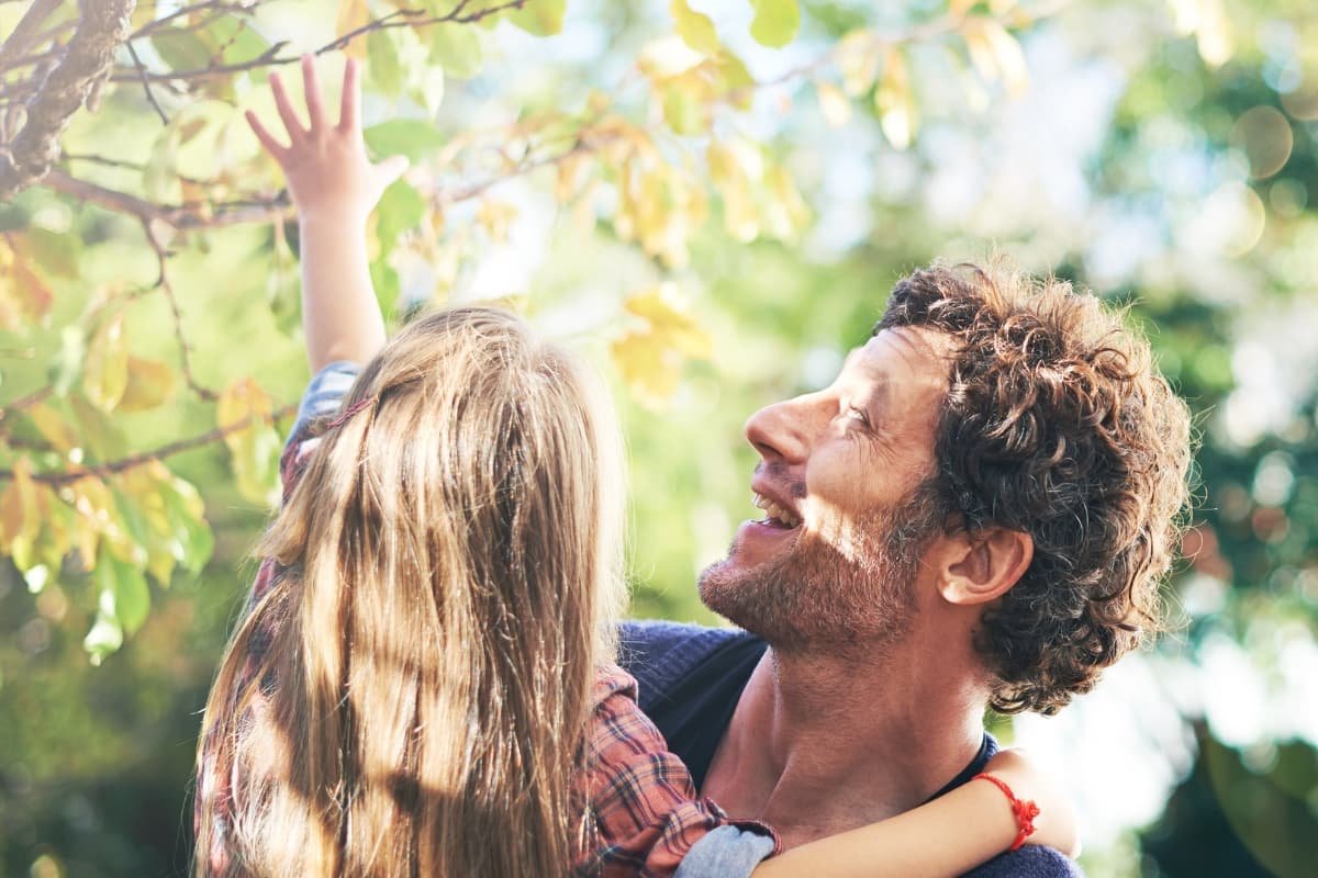 Parent and child reaching toward tree leaves together, reflecting shared wonder, presence, and connection in early childhood.