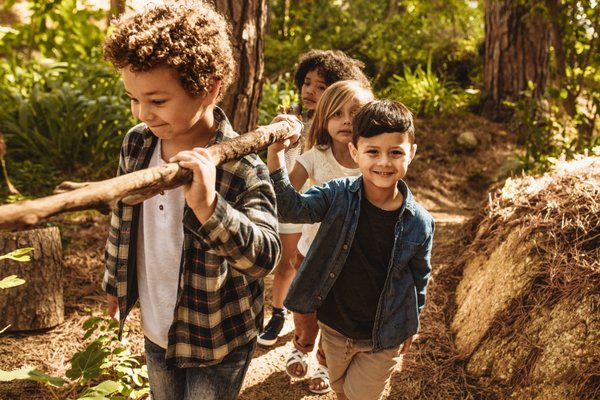 Children walking together in the forest carrying a stick, reflecting cooperation and interdependence in nature