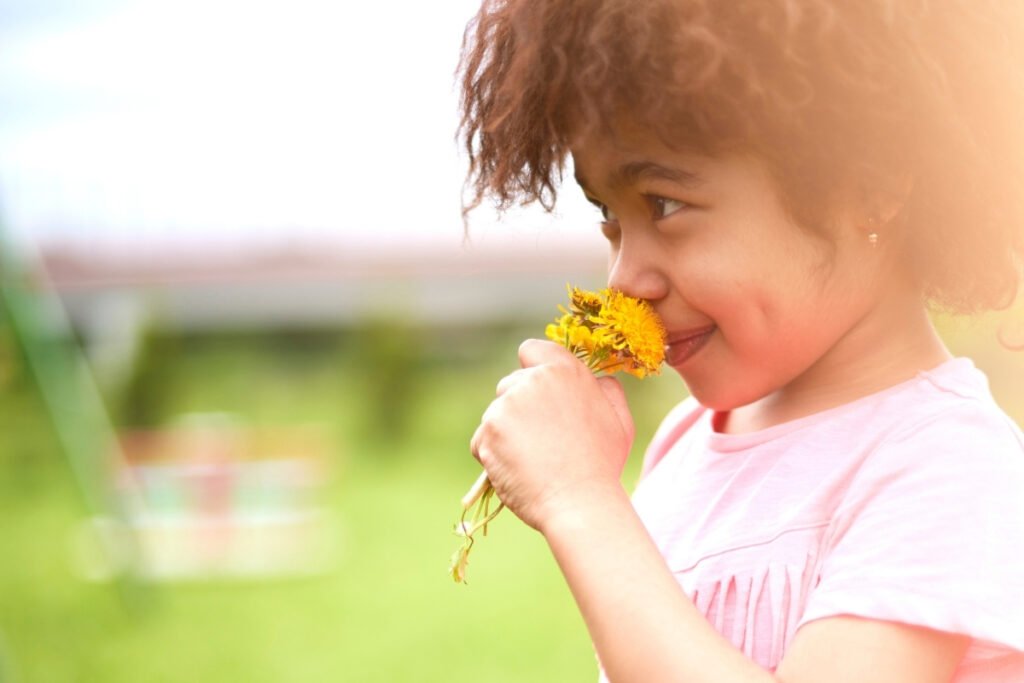 Child smelling a yellow flower outdoors, symbolizing interdependence in nature and a child’s intuitive connection to life