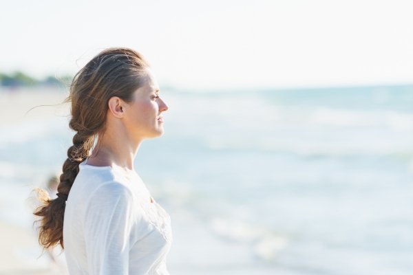 Adult standing by the ocean looking out at the water, reflecting quietly and returning to a sense of calm and presence.
