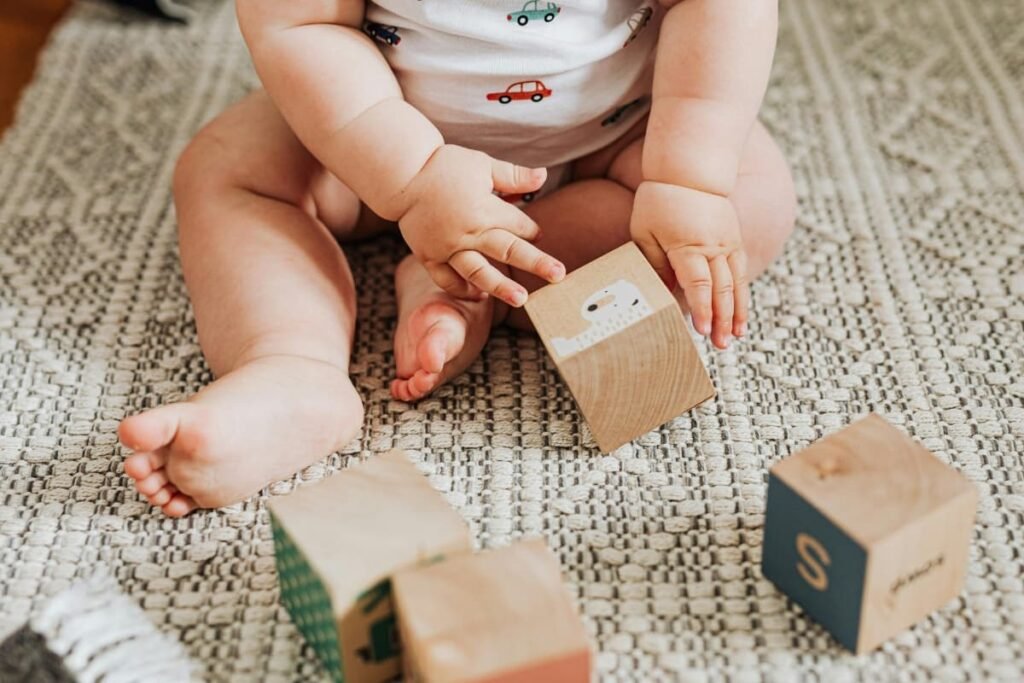 Re-membering: Sacred Wholeness as a Parenting Practice Baby seated on the floor holding wooden blocks, exploring the world through touch and curiosity.
