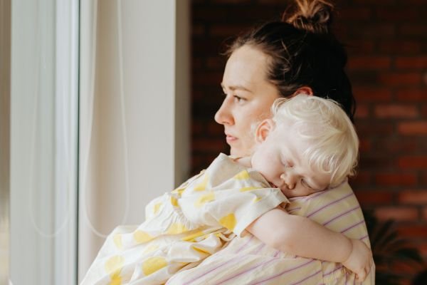 Grief in Motherhood: The Sacred Work We Rarely Name Mother holding her sleeping child by a window in a quiet moment reflecting grief in motherhood