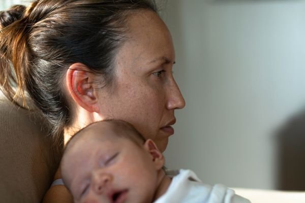 Grief in Motherhood: The Sacred Work We Rarely Name Mother holding her sleeping newborn in a reflective moment representing the identity shift after becoming a mother