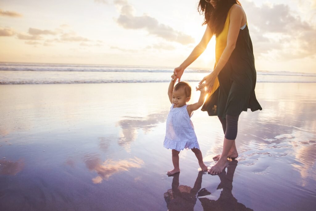 Mother and child walking on beach with reflection and sunset symbolizing re-membering, soul remembrance, and conscious parenting