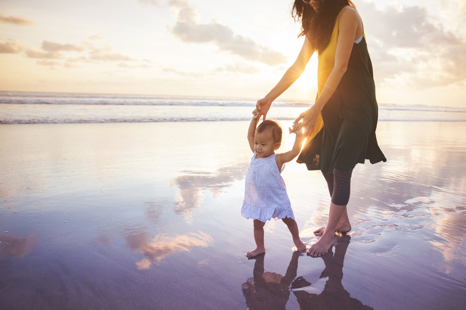 Mother and child walking on beach with reflection and sunset symbolizing re-membering, soul remembrance, and conscious parenting