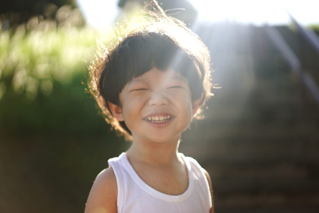 Young child smiling brightly in sunlight, capturing joy, wonder, and emotional resilience in early childhood