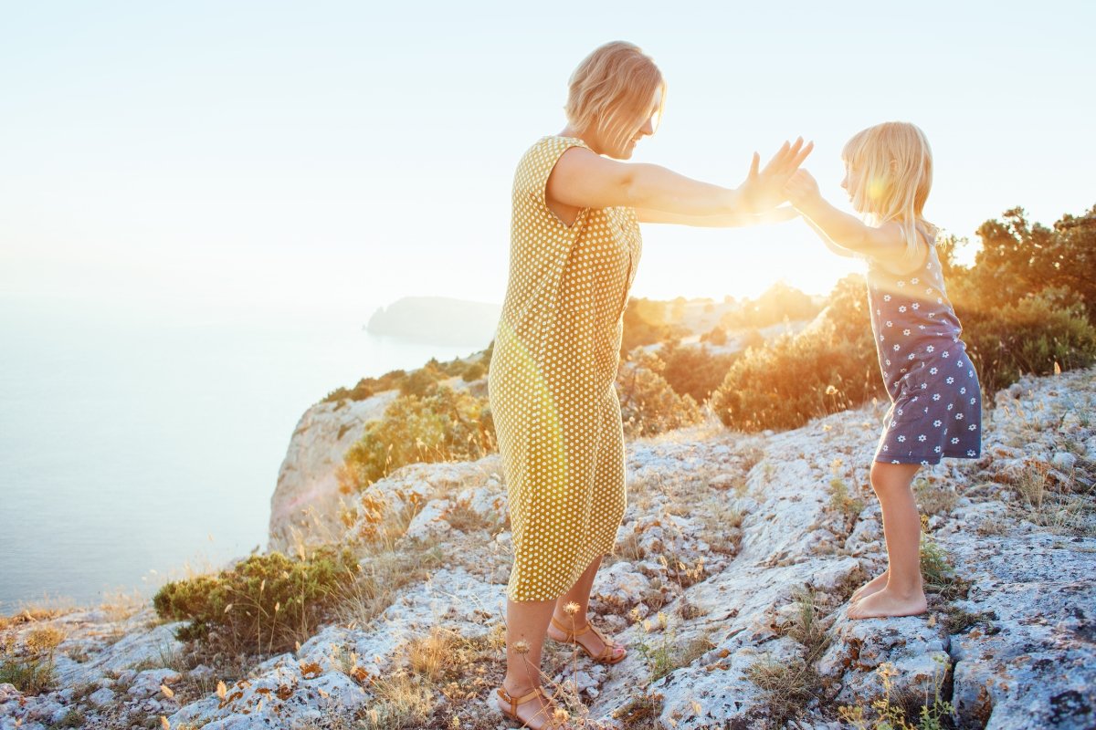 Mother and daughter holding hands on a coastal cliff at sunset, symbolizing trust, connection, and raising intuitive children