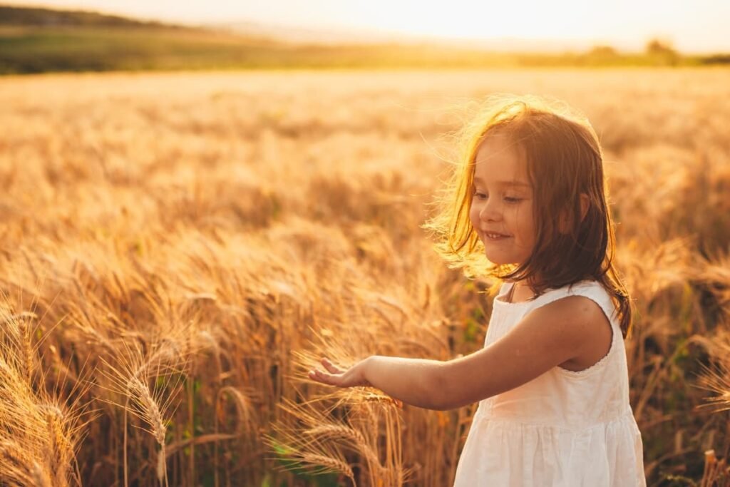 Child gently touching wheat in golden field at sunset, symbolizing connection to nature and inner guidance