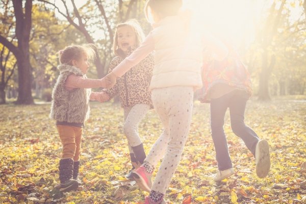 Children playing together in autumn leaves representing conscious childhood and connection to nature