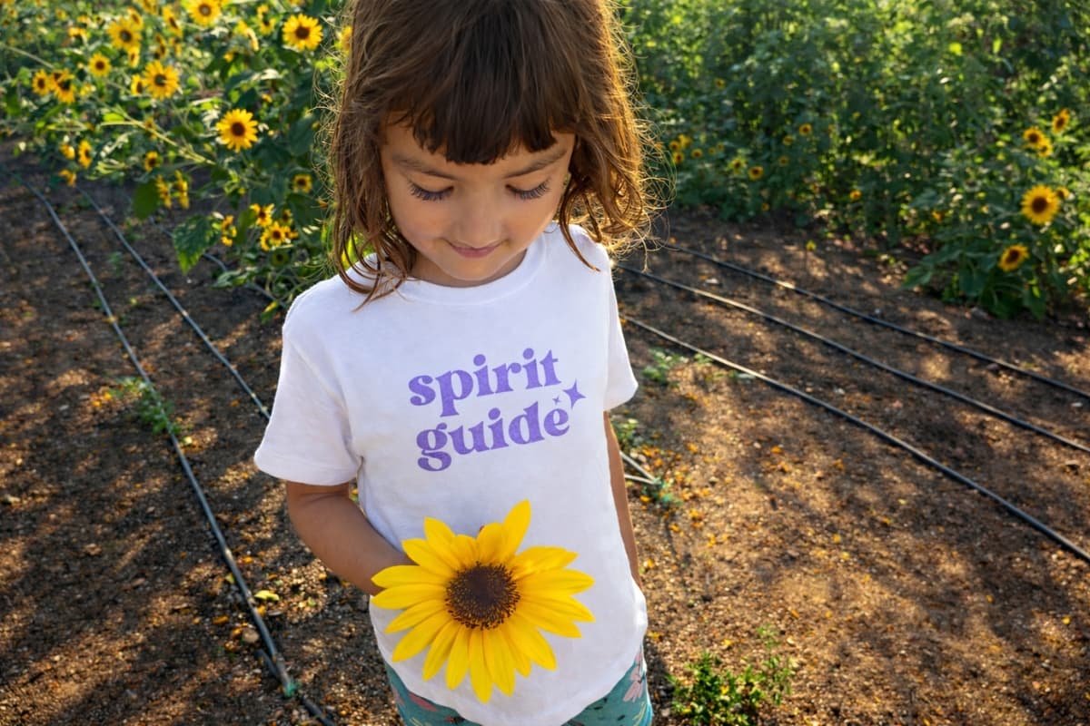 Child holding sunflower in garden wearing “Spirit Guide” shirt representing raising conscious children and connection to nature