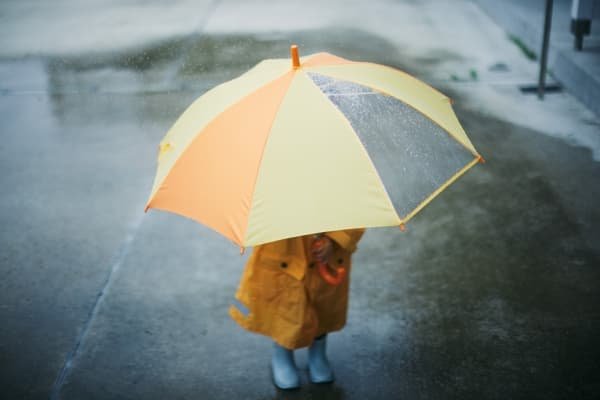 The Gifts Hidden in Our Shadow: Parenting, Healing & the Parts Our Children Reflect Child standing beneath an umbrella in the rain symbolizing emotional sensitivity and reflection in parenting and shadow work.