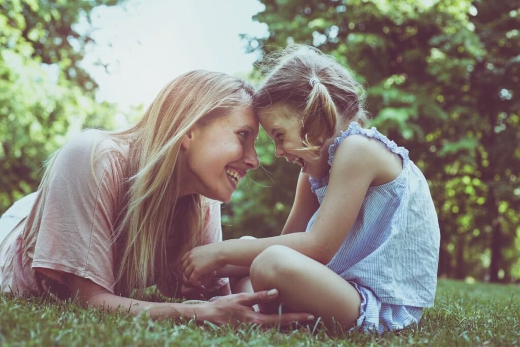Mother and daughter sharing a joyful moment outdoors representing conscious parenting, emotional healing, connection, and reparenting.