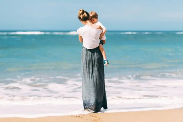 Mother holding her child by the ocean, symbolizing connection, presence, and emotional healing through parenting.