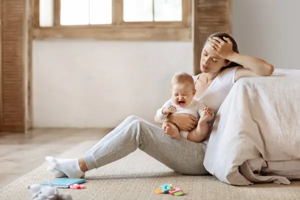 Exhausted parent holding a crying baby, illustrating the challenges of conscious parenting and intergenerational healing.