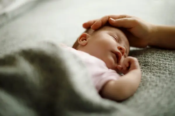 Echoes of the Stars: The Story Behind Our Children's Affirmation Cards Parent gently resting a hand on a sleeping baby during a bedtime affirmation ritual
